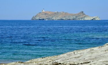 Île rocheuse avec phare dans une mer bleue, vue depuis la côte