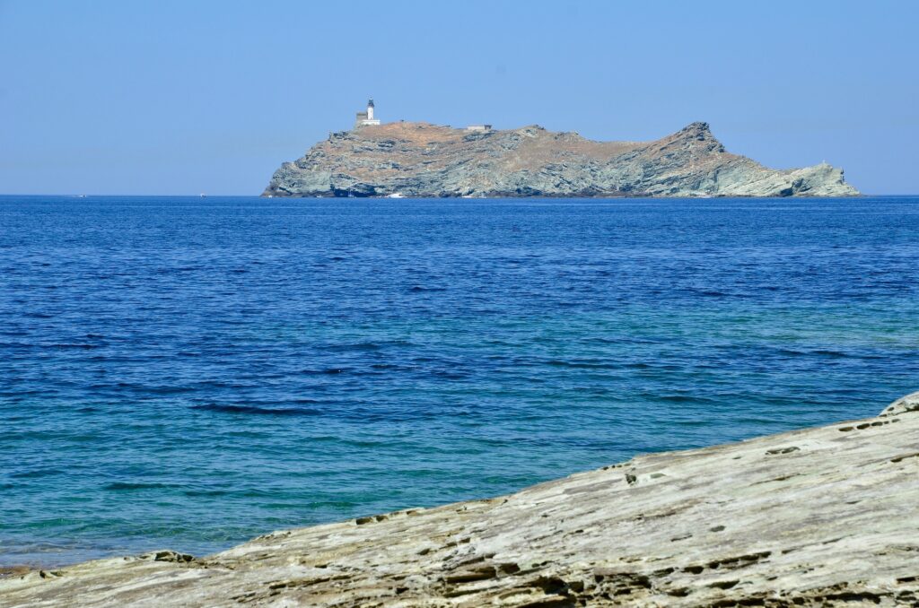 Île rocheuse avec phare dans une mer bleue, vue depuis la côte