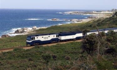 Train qui roule dans un paysage verdoyant avec la mer d'un bleu turquoise au fond.