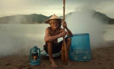 Homme tenant son pagai sur les bords d'un lac bordé de montagnes